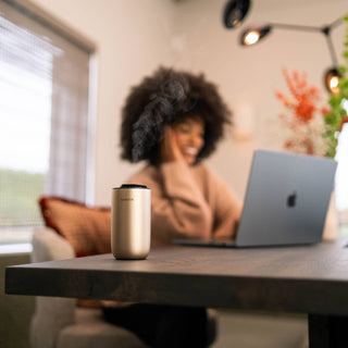 Eine Person, die an einem Tisch in einem gemütlichen Raum an einem Laptop sitzt, neben ihr steht eine Kaffeetasse.