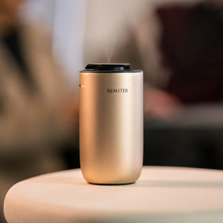 Goldfarbener Aromadiffusor mit dem Schriftzug „Aemster“ auf einem verschwommenen Hintergrund